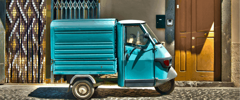 Una camioneta de reparto pequeña y colorida frente a una puerta