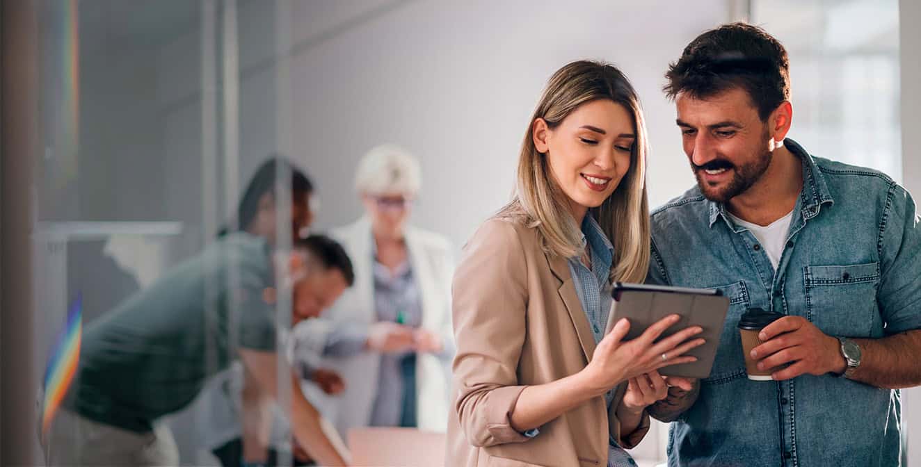 Hombre y mujer sonrientes en un entorno corporativo mirando una tableta en sus manos