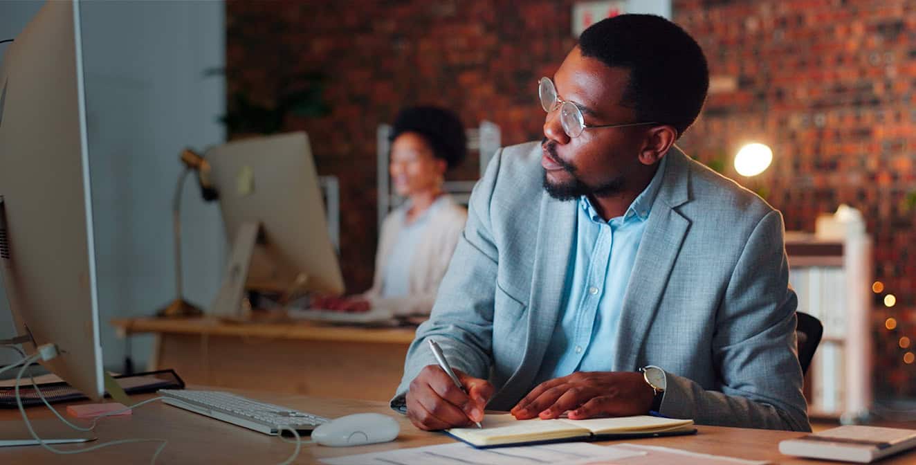 Hombre negro en un entorno corporativo sentado en un escritorio, mirando su computadora y tomando notas