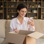 Satisfacción del cliente: mujer usando un teléfono celular mientras sostiene una caja de cartón.