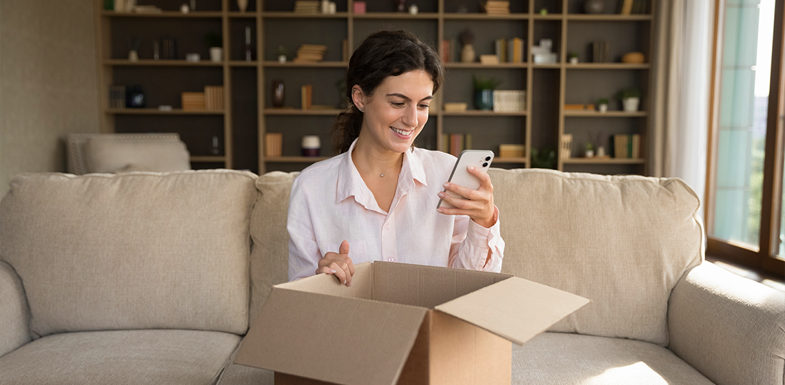 Satisfacción del cliente: mujer usando un teléfono celular mientras sostiene una caja de cartón.